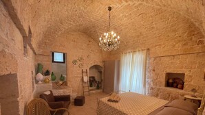 A stone-walled bedroom with a bed, a chair, a small table, and a chandelier.