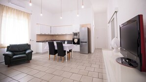 A modern kitchen with white cabinets, a stainless steel refrigerator, and a dining area with a table and chairs.