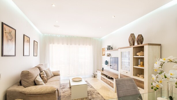 Ein modernes Wohnzimmer mit einem beigefarbenen Sofa, einem Glastisch und einem Fernseher auf einer Holzkommode.