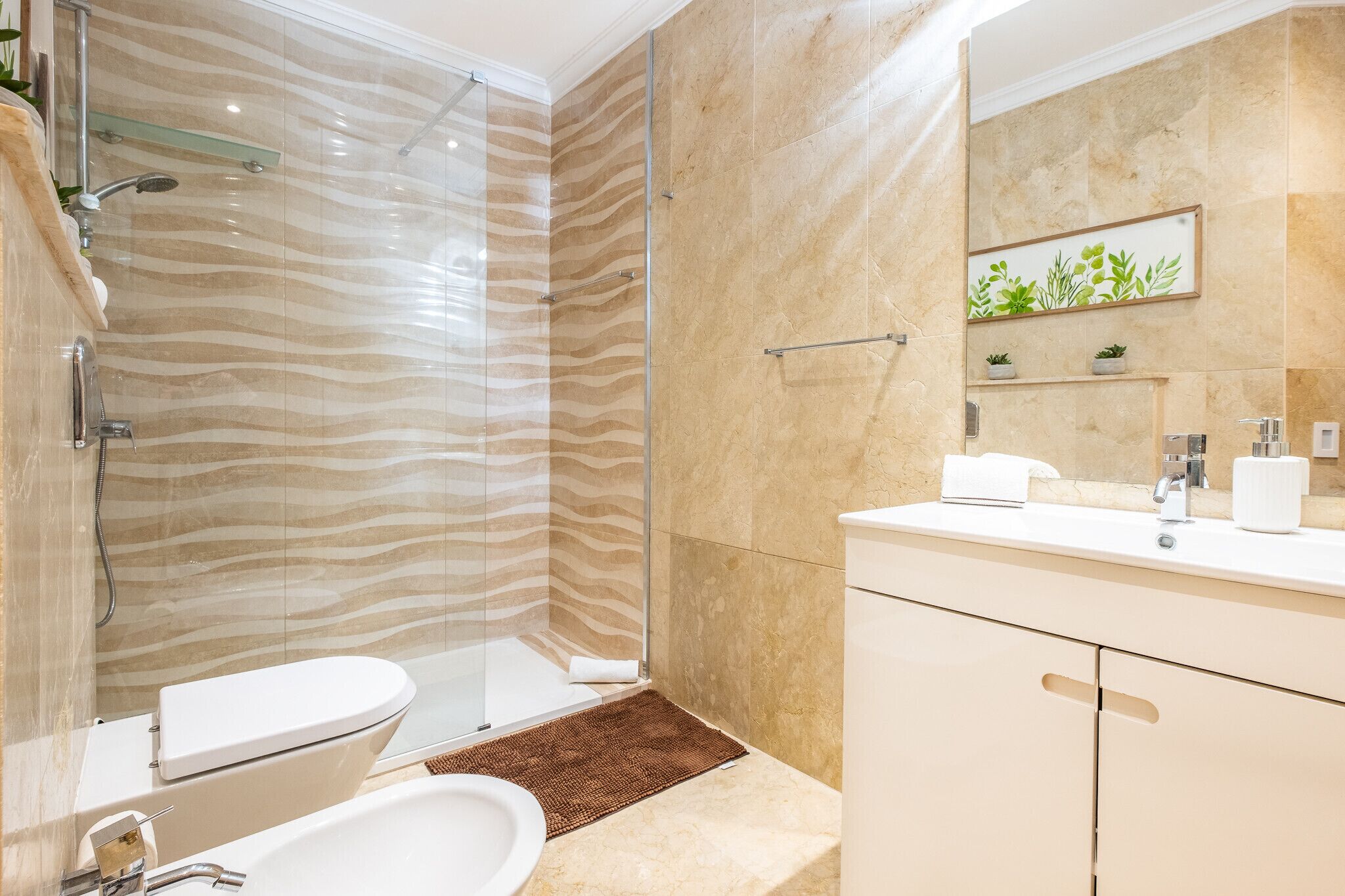 Un baño moderno con ducha envuelta en vidrio, inodoro blanco, lavamanos y espejo decorado con una planta.