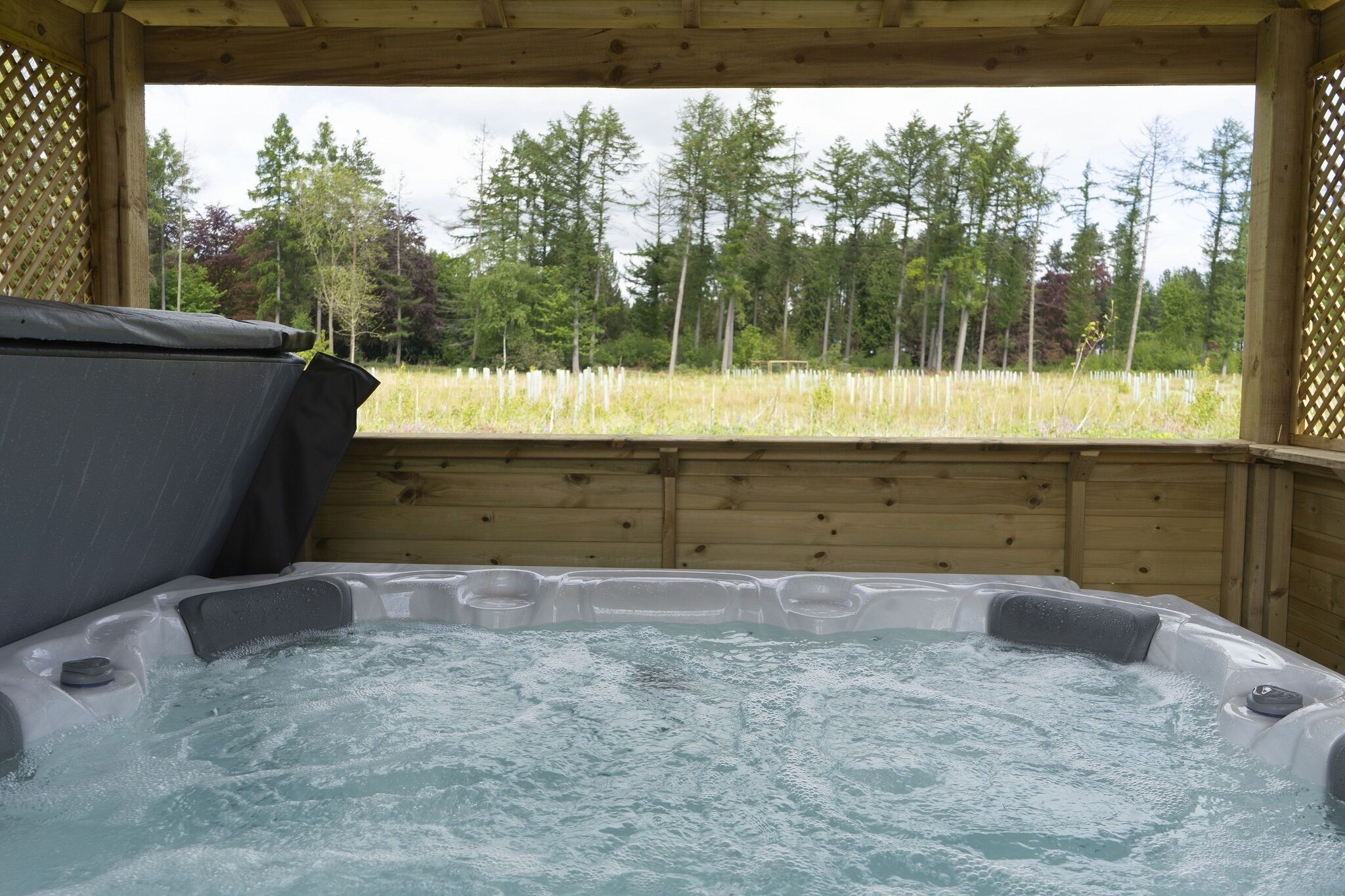 A hot tub with a wooden deck and a view of a forest.