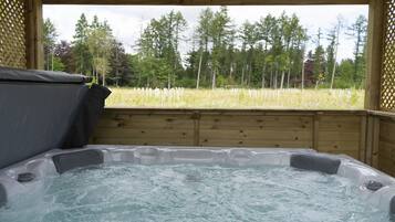 A hot tub with a wooden deck and a view of a forest.