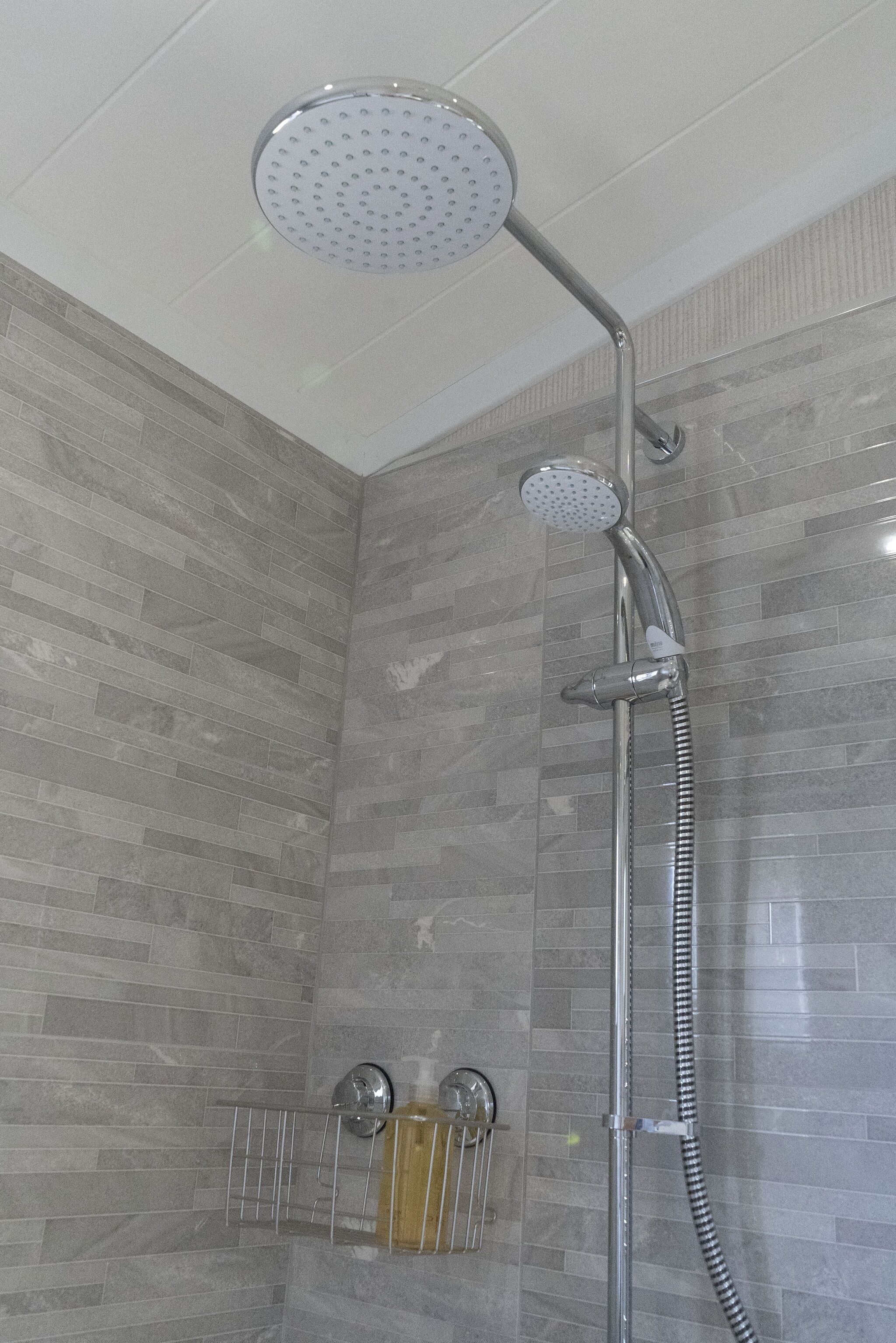 A shower with a handheld showerhead and a wall-mounted faucet, tiled walls, and a metal towel rack with bottles.