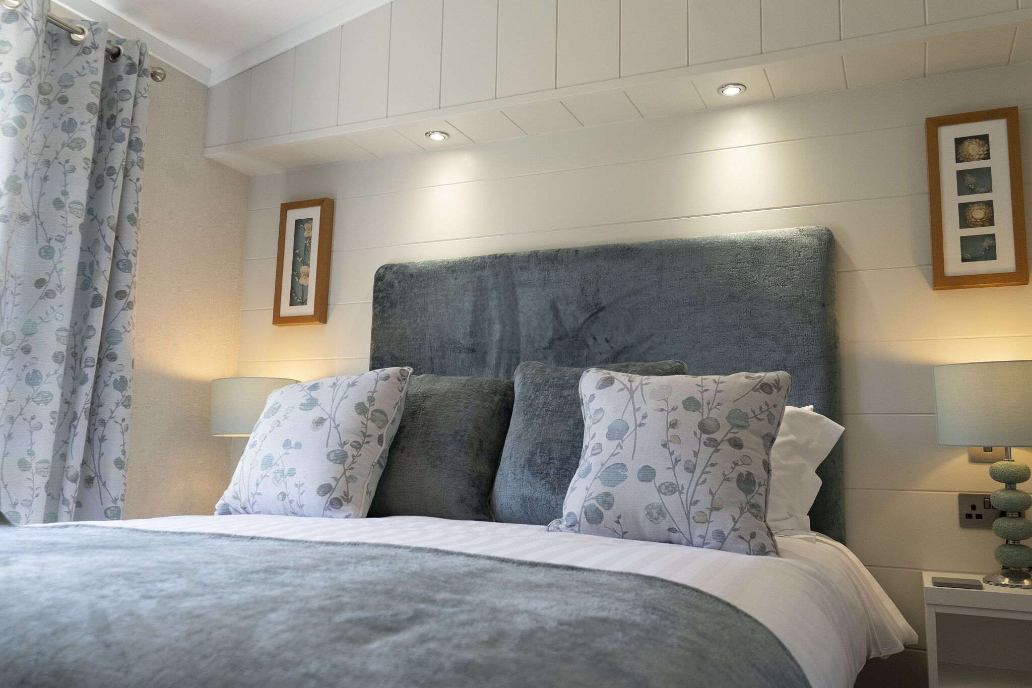 A bedroom with a large bed, a headboard, two bedside lamps, and a framed picture on the wall.