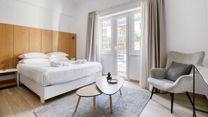 Moderni hotellihuone, jossa on sänky, pieni pöytä, tuoli ja näkymä ulkoiselle parvekkeelle.