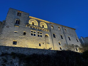 Ein aus Stein gebautes Gebäude mit zahlreichen Fenstern und Bogenöffnungen, beleuchtet von warmem Licht.