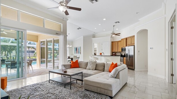 A spacious living area with a sectional sofa, a coffee table, and a large rug. There is a kitchen area with modern appliances and wooden cabinets.