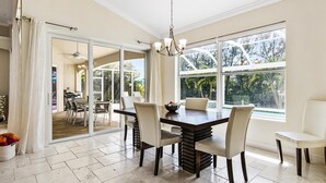 A spacious dining area with a large table and chairs, a chandelier, and a view of the outdoors through large windows.