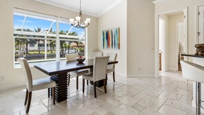 A dining area with a large window, a chandelier, and a view of palm trees.