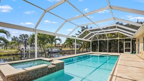 A swimming pool with a glass enclosure, surrounded by palm trees and a view of a body of water.
