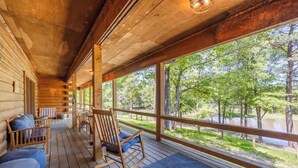 Eine Blockhütte mit Veranda, Holzschaukelstühlen und Blick auf einen See.