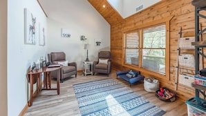 Ein gemütliches Wohnzimmer mit Holzwänden, einem großen Fenster, einem Sofa, einem Couchtisch und einem Teppich.