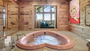 A wooden cabin interior with a heart-shaped hot tub, wooden walls, and a large window. - E.Z drive! WOW VIEWS, hotTUB 🎱 POOL TABLE, fireplace Close to Gatbg & Dollywood (Sevierville)