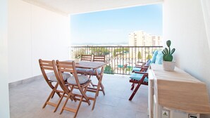 A balcony with a table and chairs, a potted cactus, and a view of buildings and mountains. - Global Vacacional: Apartment on the beach of Canet d'en Berenguer (Canet d´en berenguer)