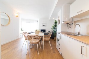 A modern kitchen with a built-in washing machine, a dining area with wicker chairs, and a large mirror on the wall.