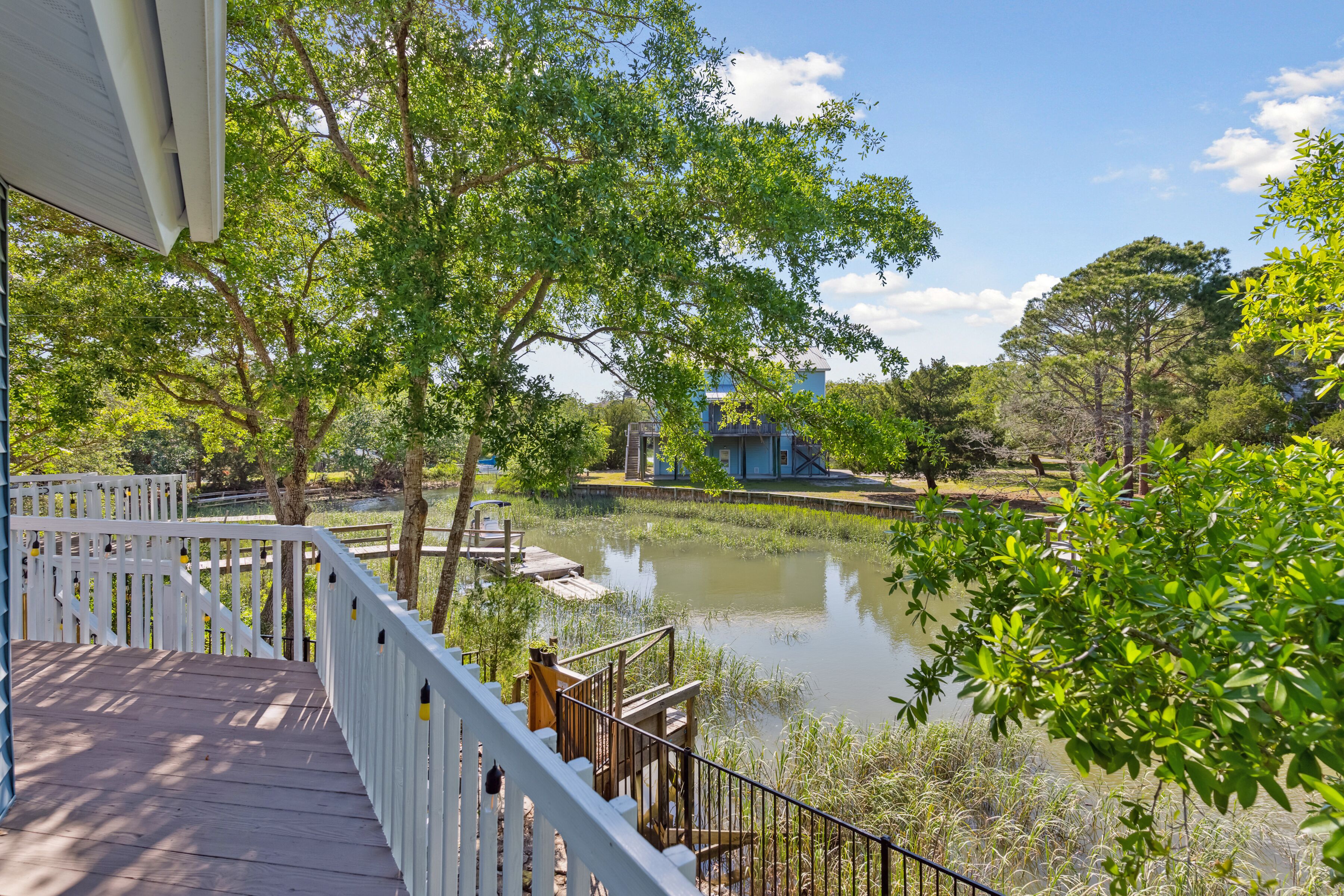A wooden deck with white railings overlooking a pond and a building in the background.