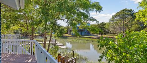 A wooden deck with white railings overlooking a pond and a building in the background.