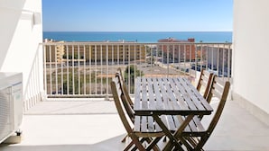 A balcony with a table and chairs, overlooking a coastal area with buildings and a clear sky.