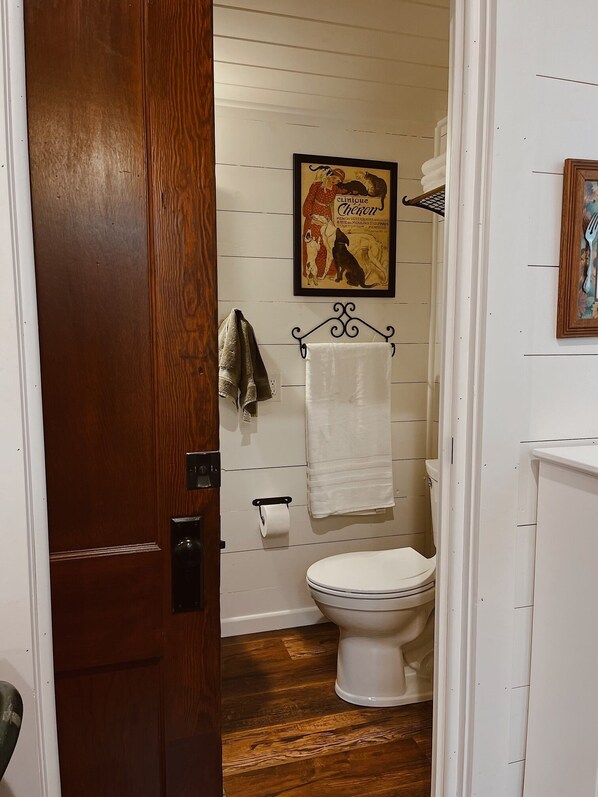 Uma casa de banho com soalho de madeira, sanita branca, porta-toalhas e um quadro emoldurado na parede.