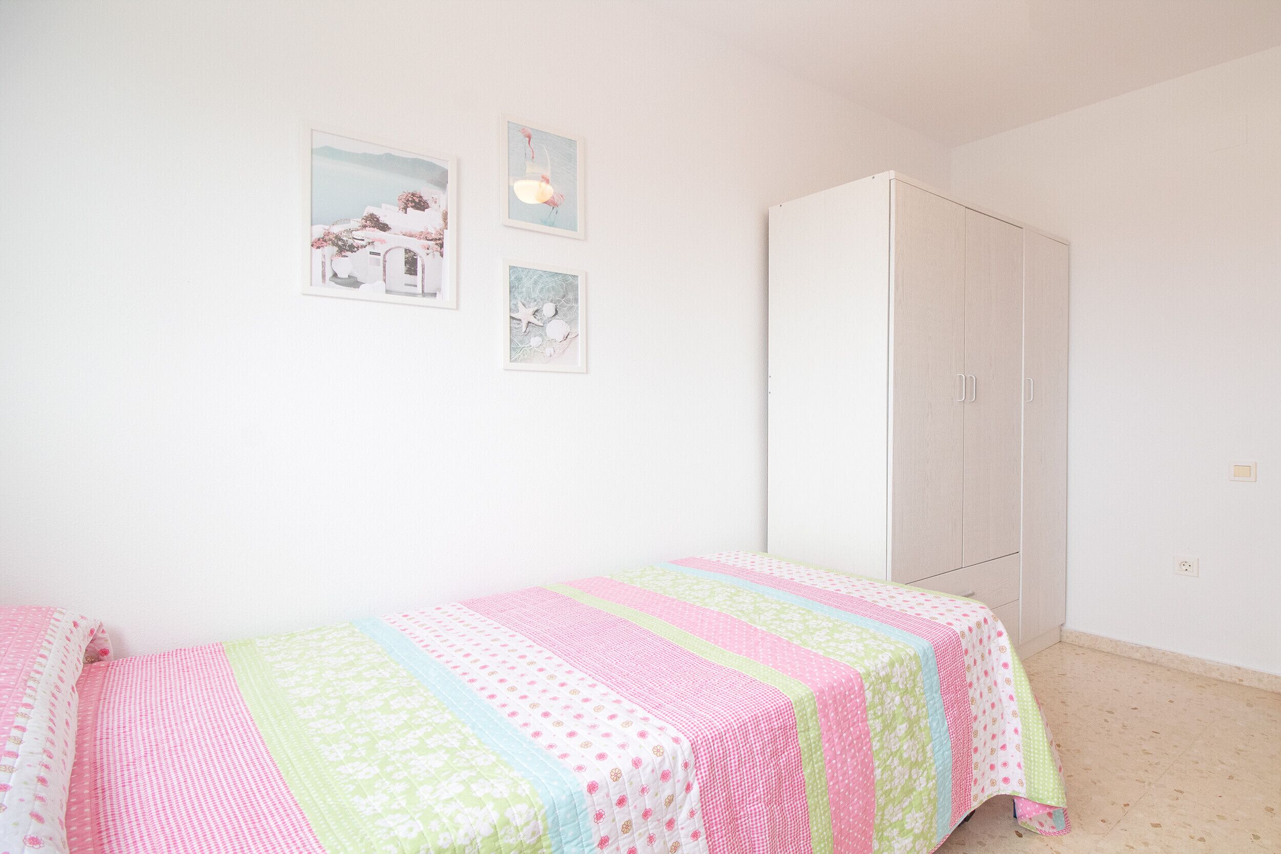 A bedroom with a bed, a wardrobe, and three wall-mounted pictures.
