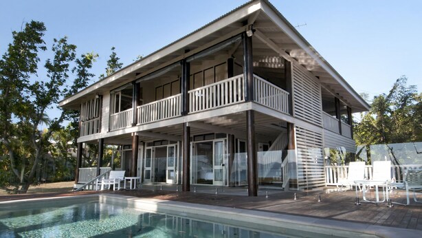 A two-story house with a balcony, a swimming pool, and outdoor furniture.