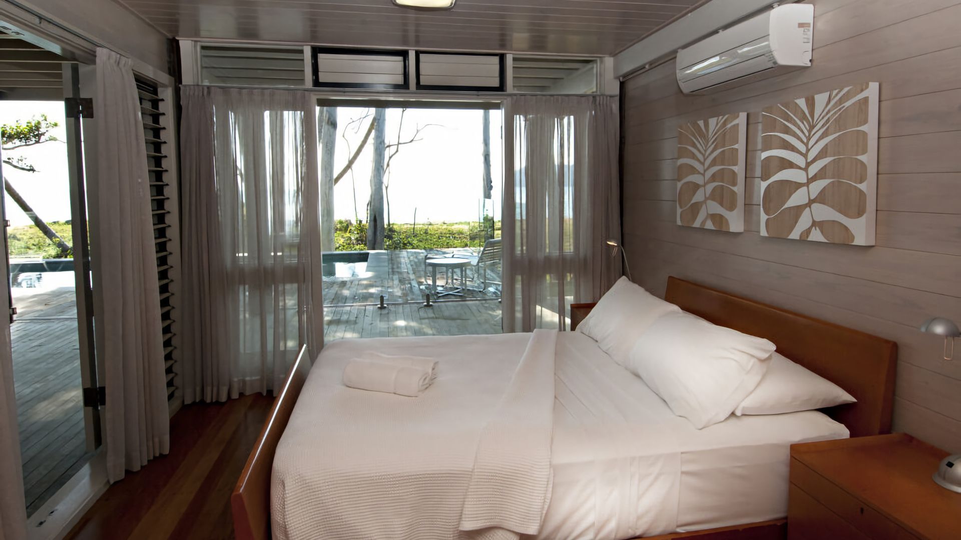 Ein Schlafzimmer mit einem Bett, einem Nachttisch und Blick auf eine Terrassenanlage.