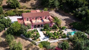 Eine große, rosa Villa mit Ziegeldach, mehreren Zimmern, einem Swimmingpool und umgebender Bepflanzung.