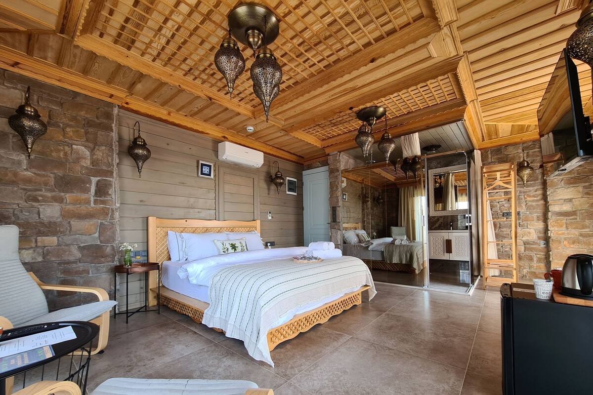 Una habitación amplia con una cama grande, techo de madera, paredes de piedra y chimenea de piedra.