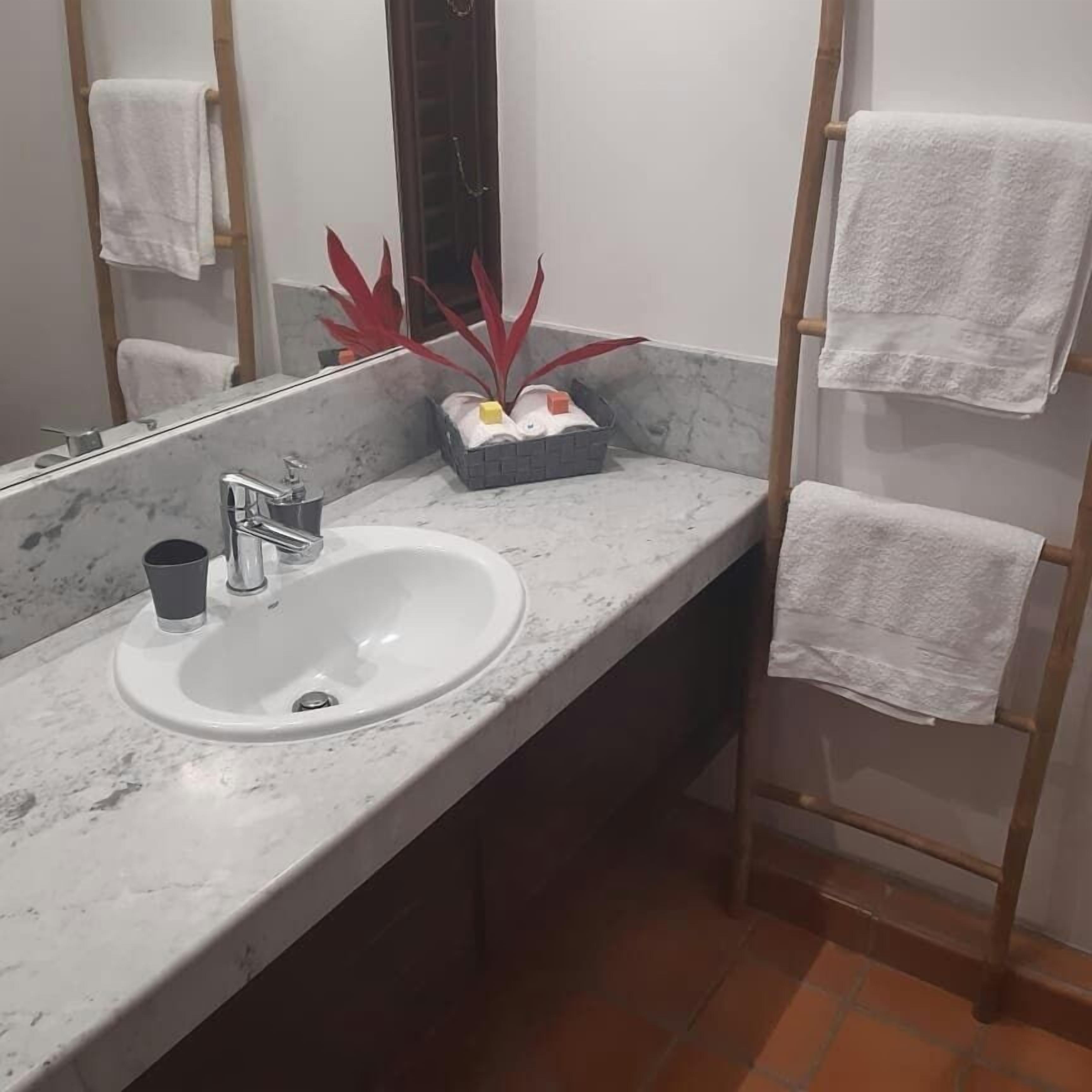 A bathroom with a marble sink, a mirror, and a towel rack with multiple towels.