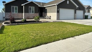 A two-story house with a garage, a well-maintained lawn, and a small patio area. - Cheerful, spacious, sunny & comfy 4-bdrm home (Rock Springs)