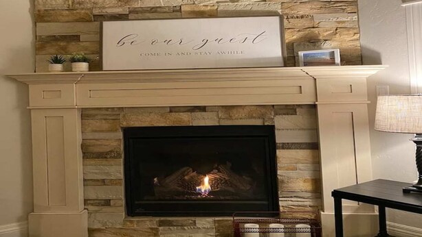 A fireplace with a stone wall above, a sign that reads "be our guest," and a small table with candles. - Cheerful, spacious, sunny & comfy 4-bdrm home (Rock Springs)