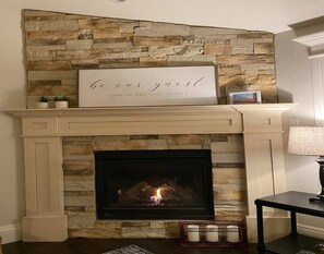 A fireplace with a stone wall above, a sign that reads "be our guest," and a small table with candles. - Cheerful, spacious, sunny & comfy 4-bdrm home (Rock Springs)