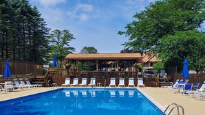 A swimming pool with lounge chairs and umbrellas, surrounded by a wooden deck and trees. - Seven Springs Mtn. Villas Condo - Ski, Golf, Hike, Sporting Clays, & Relaxation! (Champion)