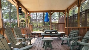 A covered outdoor seating area with wooden chairs and a picnic table, surrounded by a wooden fence and trees. - Seven Springs Mtn. Villas Condo - Ski, Golf, Hike, Sporting Clays, & Relaxation! (Champion)