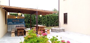 Eine Terrasse im Freien mit Holztischen und -bänken, einer Steinkaminanlage und einer blauen, mit Fliesen verkleideten Wand.