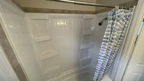 Una ducha a nivel del suelo con puerta de vidrio, una barra de metal y una cortina de ducha a rayas.