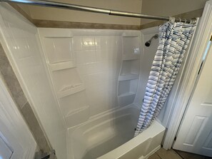 Shower features a shelf, handheld showerhead, and safety grab bar.