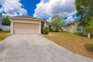 Une maison de plain-pied avec une porte de garage beige, une pelouse bien entretenue et un arbre aux fleurs blanches.