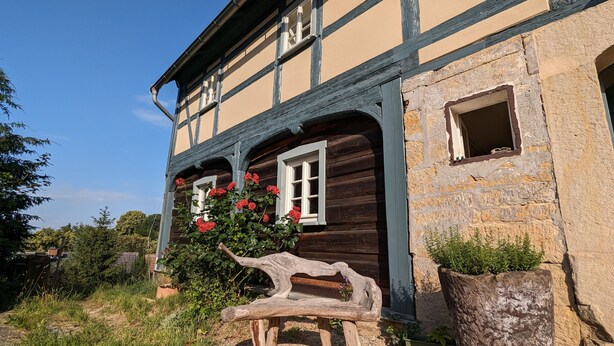 Ein traditionelles Fachwerkhäuschen mit Steinwand und einer hölzernen Bank im Vordergrund.