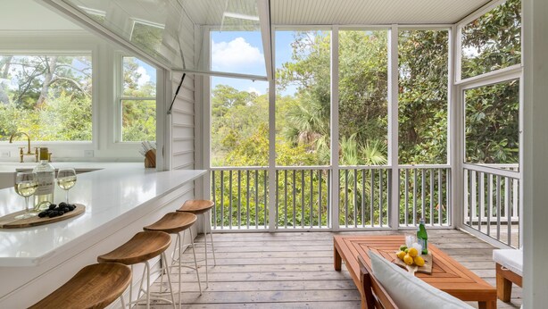 A spacious balcony with a wooden deck, a white railing, and a view of lush greenery. - Tulum-inspired coastal retreat w/ private pool, hot tub & yoga porch (Folly Beach)