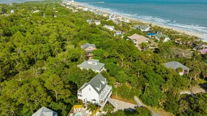An aerial view of a coastal residential area with houses surrounded by dense greenery, a beach, and a clear view of the ocean. - Tulum-inspired coastal retreat w/ private pool, hot tub & yoga porch (Folly Beach)