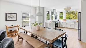 A modern kitchen with white cabinetry, a wooden dining table, and pendant lights. - Tulum-inspired coastal retreat w/ private pool, hot tub & yoga porch (Folly Beach)