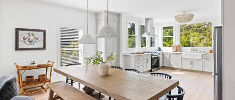 Una cocina moderna con armarios blancos, una mesa de comedor de madera y luces colgantes.