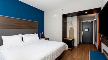 A modern hotel room with a large bed, a bedside table, a desk, and a TV.