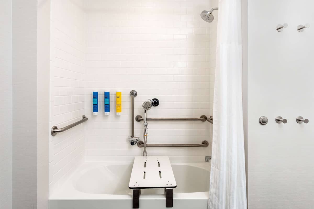 Un baño moderno con una bañera blanca, barras de apoyo y un cabezal de ducha.