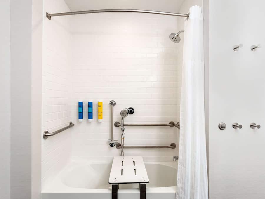 A modern bathroom with a white bathtub, grab bars, and a showerhead.