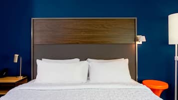 A neatly made bed with white linens and a wooden headboard, a bedside table with a lamp, and an orange chair in a room with blue walls.