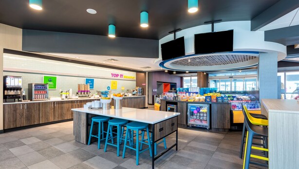 Un café moderno con una isla central, taburetes de bar, un mostrador refrigerado y una estación de bebidas 'Top It'.
