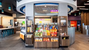 Zona de mercado abierta las 24 horas, con opciones de bocadillos y desayuno, estación de café y mostrador visible para ordenar.