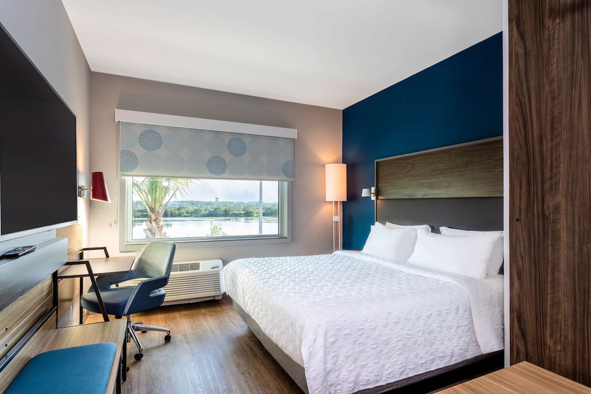 Habitación de hotel con cama, escritorio, silla, ventana con vistas y televisor montado en la pared.